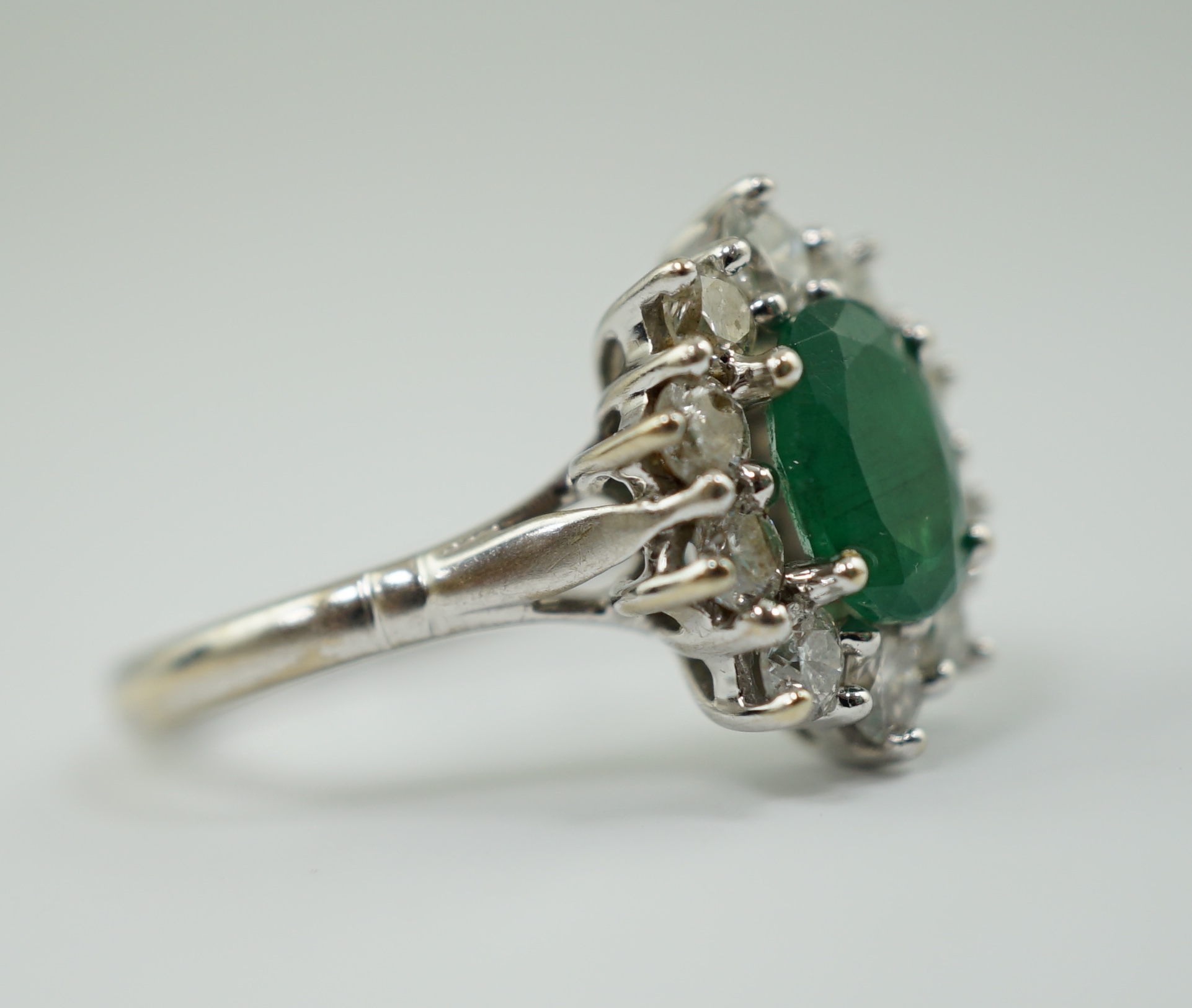 A modern 18ct white gold, single stone oval cut emerald and ten stone diamond set oval cluster ring